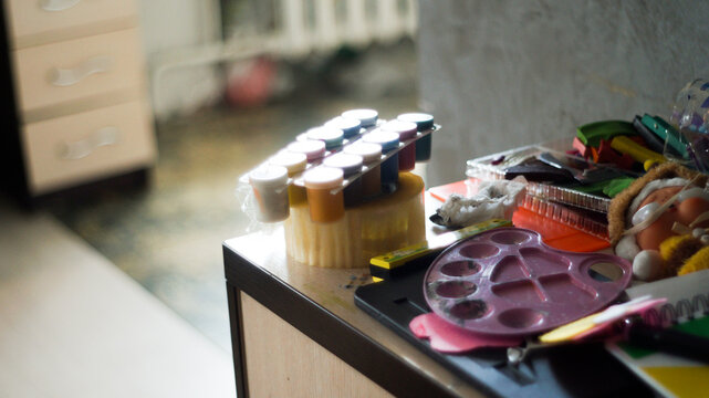 Creative mess with messy paint brushes and multi-colored paints on artist tabletop