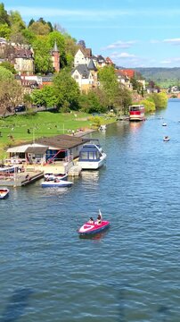 Boats move on a river in a town with houses and trees near the water on a sunny day