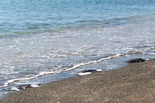 Close-up of a transparent sea wave crashing onto a sandy beach. The sun sparkles on the water surface. Sea surf on a sunny day. Transparent clean water of the Black Sea. Atmosphere of summer vacation