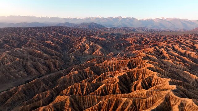 Aerial view of the rugged, eroded canyons and ridges of Ak Say illuminated by golden hour light in Ak Say, Issyk-Kul Region, Kyrgyzstan.