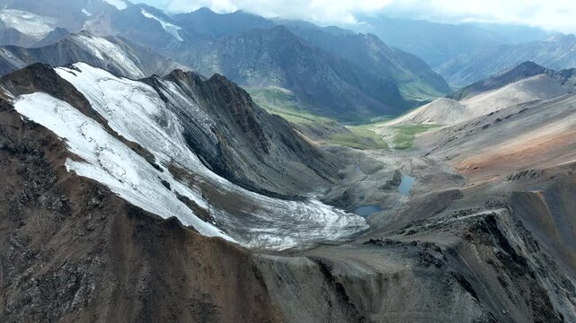 Aerial view of the Chon Ashu Pass featuring a large glacier, rugged rocky slopes, and alpine lakes in Karakol, Issyk-Kul Region, Kyrgyzstan.