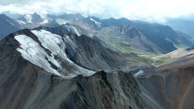Aerial view of the rugged Chon Ashu pass featuring snow-capped peaks, rocky slopes, and glacial valleys in Karakol, Issyk-Kul Region, Kyrgyzstan.