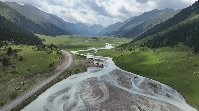 Aerial view of the winding river through the lush green valley of Chon Ashu Pass with mountains and a road in the background in Karakol, Issyk-Kul Region, Kyrgyzstan.