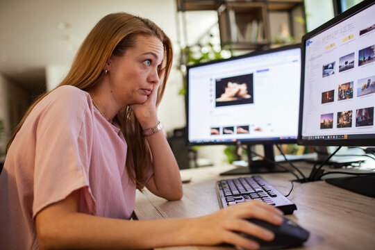 Tired woman editing photos on dual monitors in home office