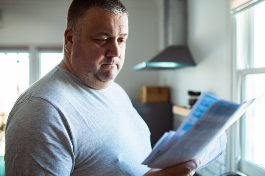 Worried man reading household bills in kitchen