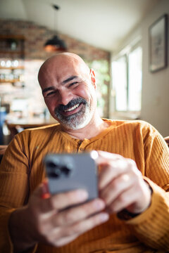 Smiling middle-aged man using smartphone at home