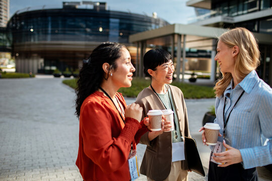 Three businesswomen networking with coffee outside office campus