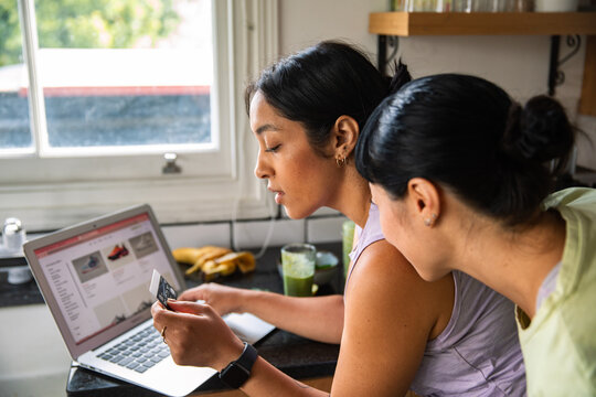 Two women shopping online with credit card in home kitchen