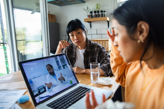 Two women on a telehealth video call at the kitchen table