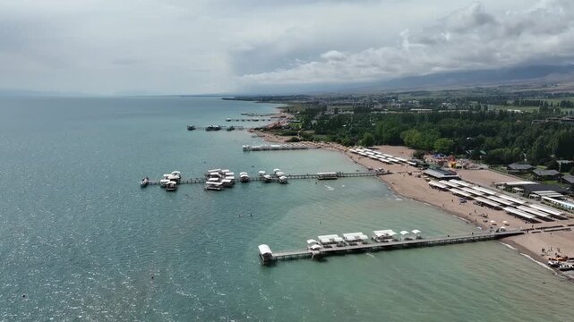Aerial view of Issyk Kul lake with wooden piers, white sunshades, and sandy beach in Cholpon Ata, Issyk-Kul Region, Kyrgyzstan.