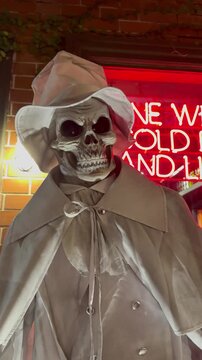 Static shot of spooky animatronic skeleton figure swaying with blinking red eyes in a Halloween display, vertical video.