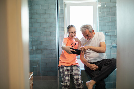 Grandfather and granddaughter brushing teeth and taking a selfie in home bathroom
