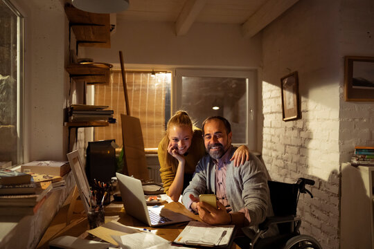 Smiling wheelchair user and woman working at home office at night