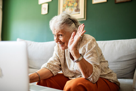Smiling senior woman video chatting on laptop at home