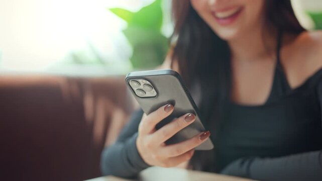 Close up of smiling young Asian woman using smartphone while relaxing at cafe, browsing mobile app and social media on touchscreen, digital communication, online lifestyle and modern technology