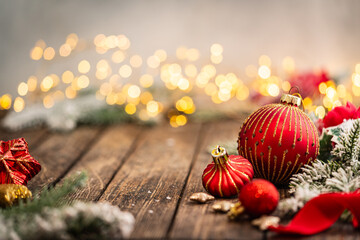Naklejka premium A Christmas background featuring red baubles with golden glitter stripes, a star ornament, and frosted pine on a wide rustic wood table, warmly lit with twinkling lights and copy space.