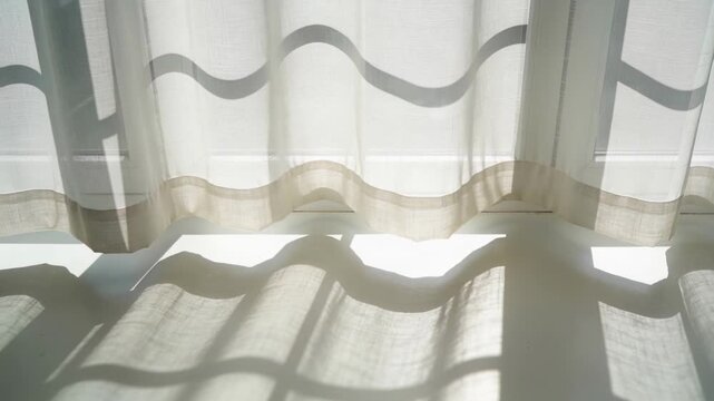 Rippling sheer curtain casting wave shadows on floor at window, sunlight moving over window frame