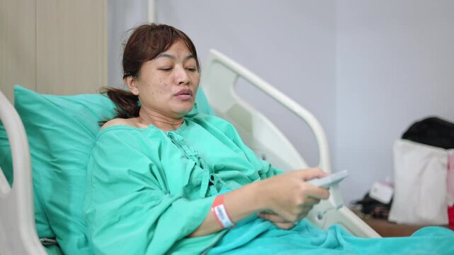 Patient relaxing on hospital bed holding tv remote device