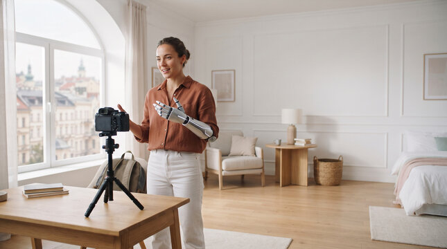 Woman with prosthetic arm recording video with camera in bright apartment