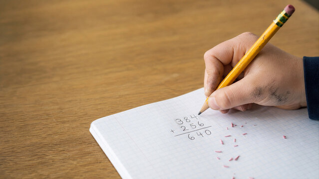 Child Hand Writing Math Equations with Pencil on Grid Paper - Primary School Education Macro - Classroom Workbook Banner - Natural Window Daylight