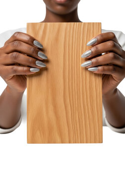 Close-up of adult woman's ebony hands with silver glitter manicure presenting a rectangular wooden sign on a transparent studio background with copy space. Concept for product mockup