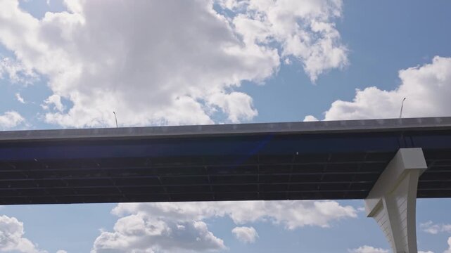 Aerial moving dolly shot of highway interstate 70 underpass looking up beneath multilane roadway with white fluffy clouds and summer sunny sun as concrete traffic structure stands tall