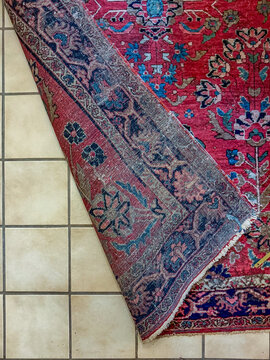 Folded corner of antique Persian wool rug on tiled floor