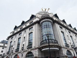 Naklejka premium Historic commercial building with grand curved glass bay and classical architecture in London, UK, elegant stone facade and rooftop sculptures against a pale sky