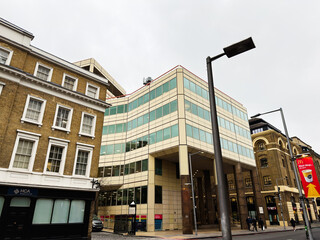 Naklejka premium Modern Cottons Centre office building and historic brick facades on a busy London, UK street with pedestrians, street lamps and urban architecture