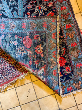 Folded corner of blue Persian wool rug on tiled floor