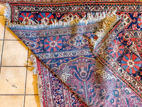 Folded corner of Persian wool rug with fringe on tiled floor