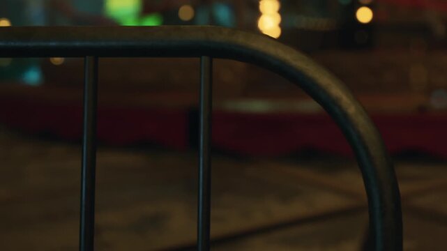 A metal gate stands in a dimly lit room, showing a close view of the lock. The background is blurred with faint hints of red and green lighting. This scene may suggest a transition or entry point.