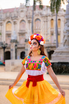 Catrina woman posing in traditional Mexican dress and makeup, celebrating the Day of the Dead with colorful flowers in her hair, standing in front of the Capitol building in Havana, Cuba