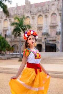 Young woman portraying a traditional Catrina, wearing colorful attire and skull makeup, posing outdoors in front of an historic building in Havana, Cuba