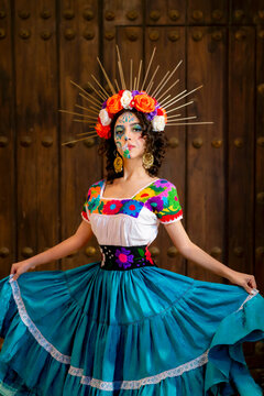 Latina woman portraying La Catrina with vibrant skull makeup and a floral crown, wearing a colorful traditional dress and standing in front of an old wooden door in Havana, Cuba
