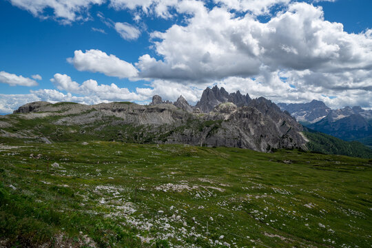 Alpine landscape with rugged dolomite peaks under a bright blue sky and fluffy white clouds, mountains