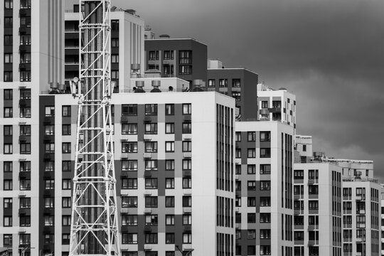 Monochrome view of modern apartment buildings with visible construction tower, repetitive windows, urban density under dramatic cloudy sky.