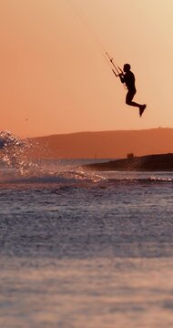 Kite surfer jumping high above the ocean with kite against a sunset sky
