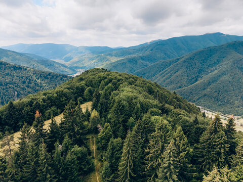 Aerial view of densely forested mountain ridges and a deep green valley beneath dramatic summer clouds.