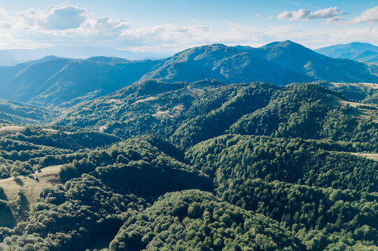 Expansive aerial panorama of lush wooded valleys and rolling mountain slopes glowing in late-day sunlight beneath a bright blue sky.