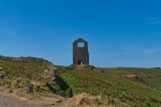 A stone mine engine house ruin stands on a verdant hill beneath a clear blue sky - Wheal Edward & Engine House, Botallack, Cornwall, UK