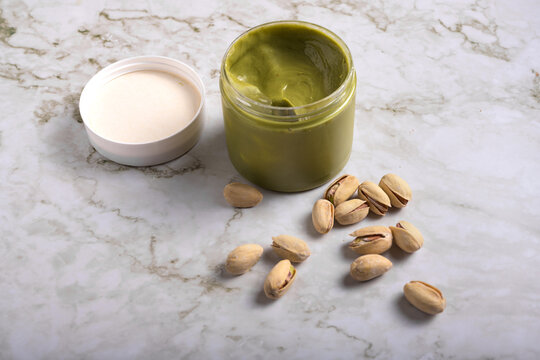 jar of creamy pistachio butter with whole nuts on marble surface, gourmet food concept, copy space