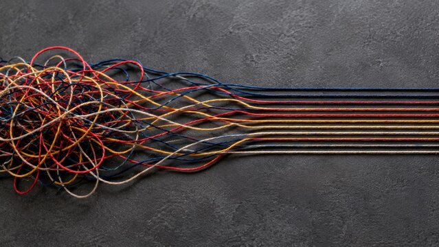 Tangled colorful threads untangling into straight parallel lines on dark slate background representing problem solving process. Concept of untangle, chaos to order. Copy space.