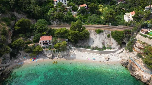 Aerial drone view of Plage des Pissarelles nudist naturist beach hidden cove with turquoise clear sea, dramatic rocky cliffs and yacht in Cap d'Ail, French Riviera, France 