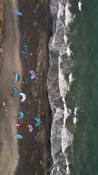 Aerial Top-Down View of Kitesurfing Kites on Dark Sand Beach and Waves
