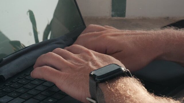Male hands typing on a laptop keyboard, representing a digital nomad working remotely outdoors