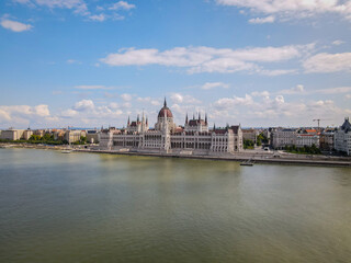 Fototapeta premium Hungarian Parliament Building and Danube River under a Bright Blue Sky with White Clouds