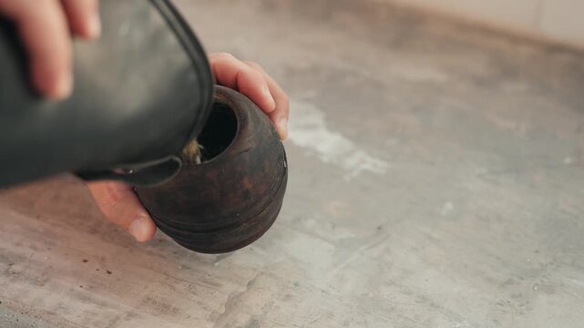 Man's hands pouring traditional south american mate tea into a wooden calabash cup on a concrete table