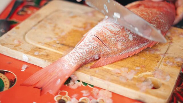 Woman's hands scaling and cutting a whole red snapper on a wooden board for cooking