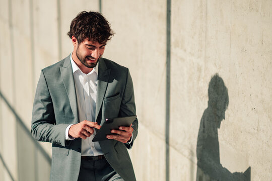 Professional businessman smiling while using a digital tablet outdoors, connecting with modern technology and remote work
